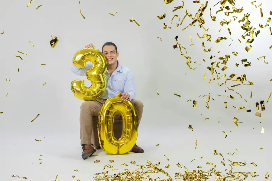 A man celebrating his 30th birthday with gold number balloons and confetti