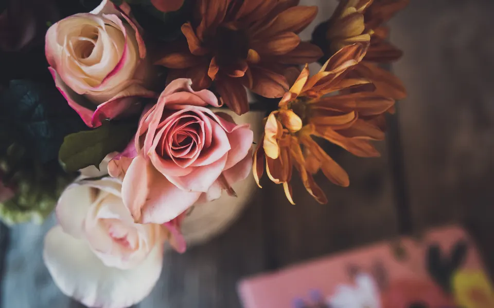 A bouquet of pink roses and orange autumn mums on a wooden table
