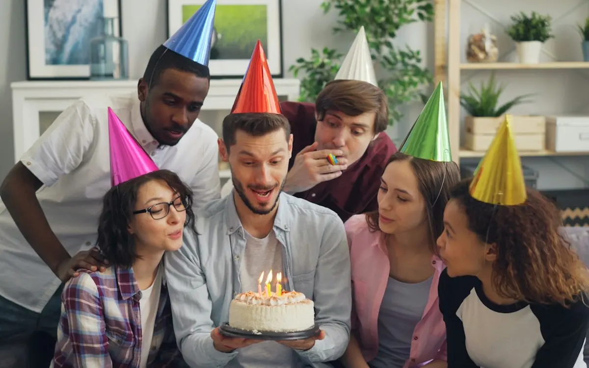 Friends in party hats surprising someone with a birthday cake