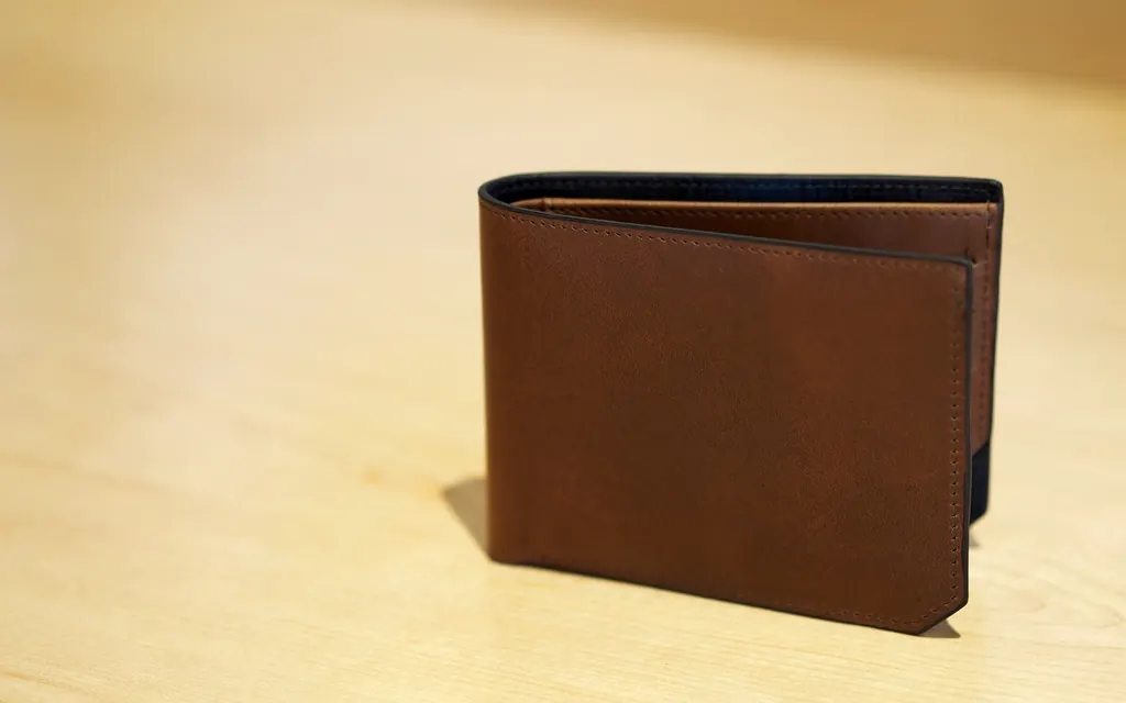A brown leather bifold wallet standing on a light wooden table