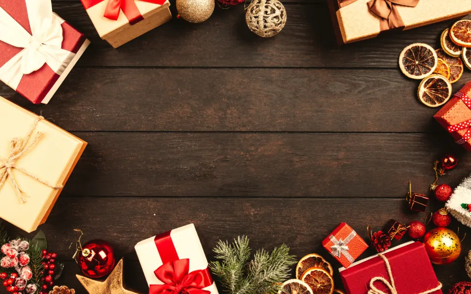 Wrapped Christmas presents with red and gold ribbons around the edges of a dark wooden table