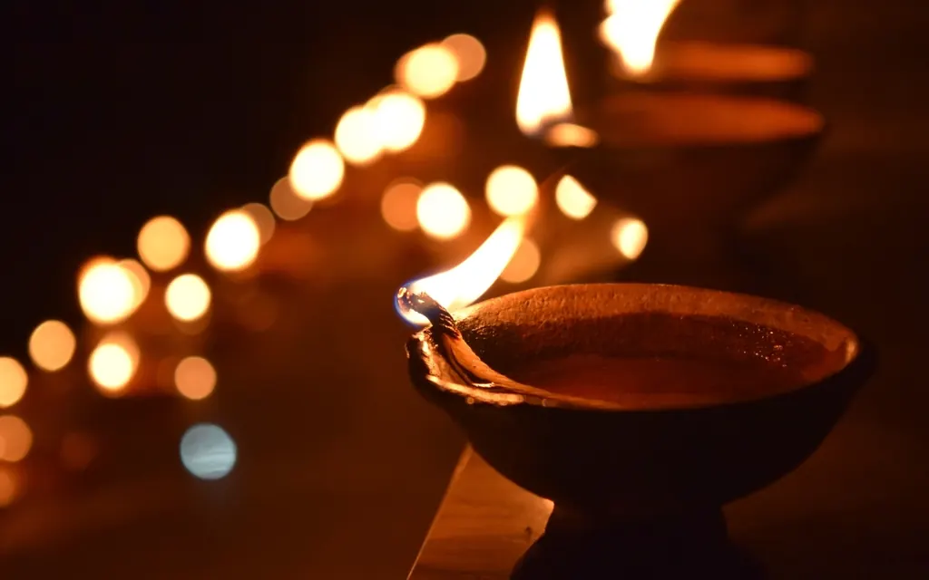 A lit clay diya in front of a row of glowing lamps