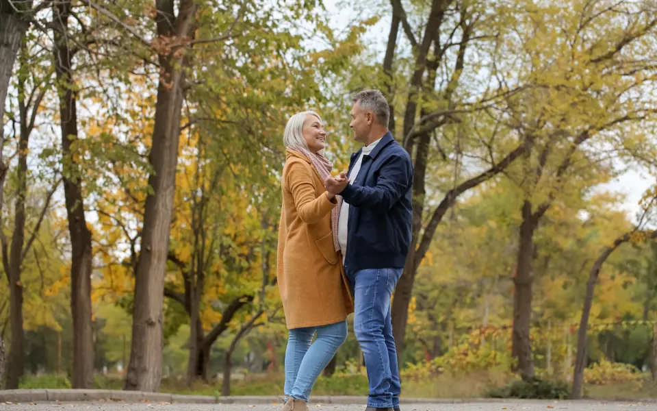 A couple in coats laughing together in a park full of autumn trees