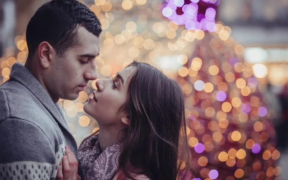 A couple about to kiss in front of blurry Christmas lights