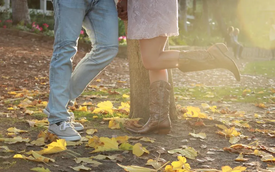 A couple standing close among fallen yellow leaves, she is on her toes in cowboy boots
