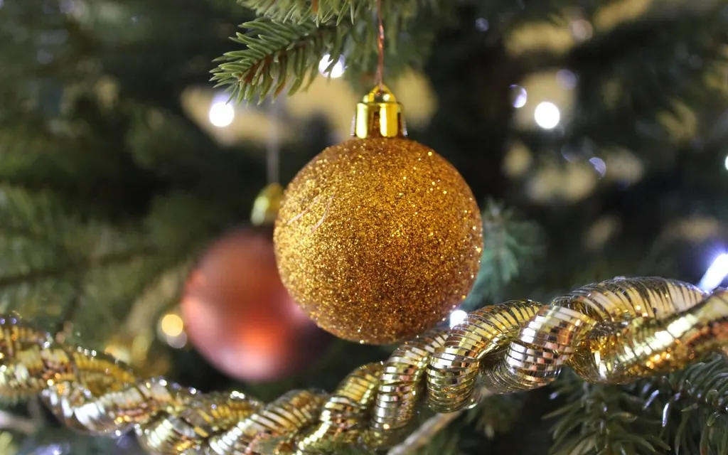 A gold glitter ornament hanging on a Christmas tree next to gold tinsel and soft lights