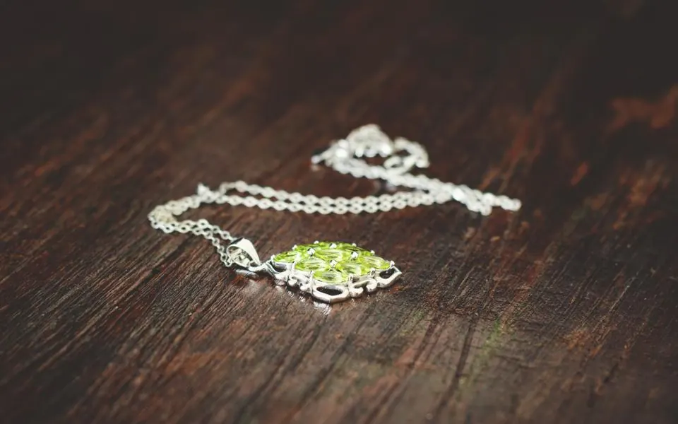 A silver necklace with a green stone pendant lying on a dark wooden table