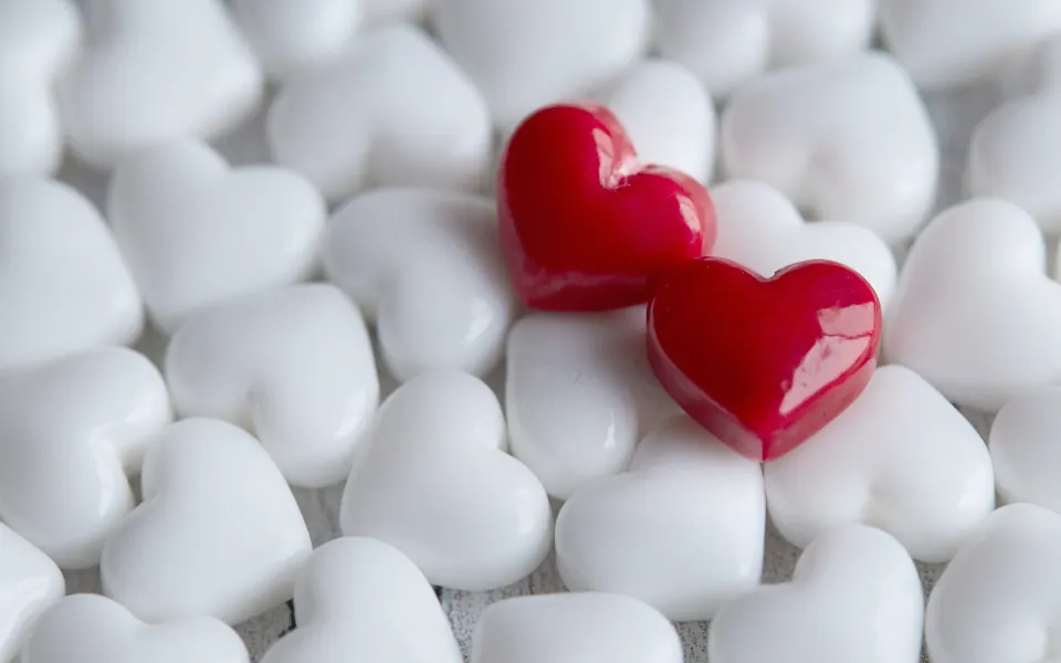 Two red heart-shaped candies on a pile of white heart candies
