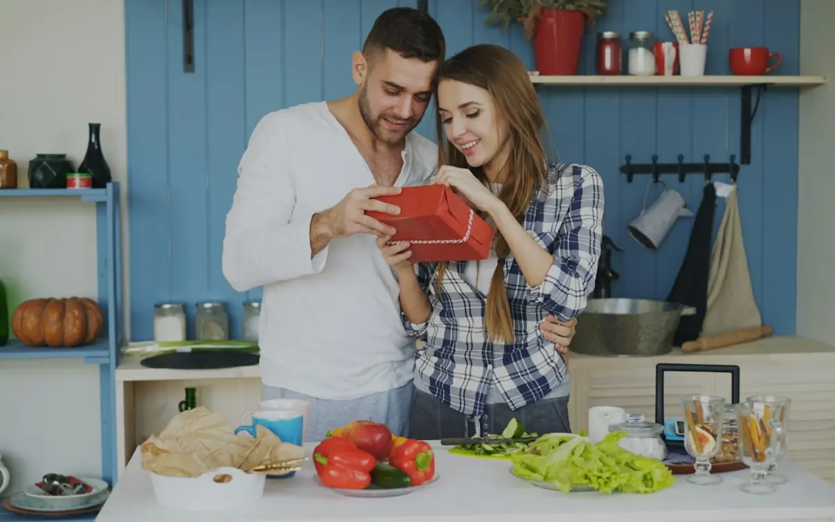 A couple opening a birthday gift together in their kitchen