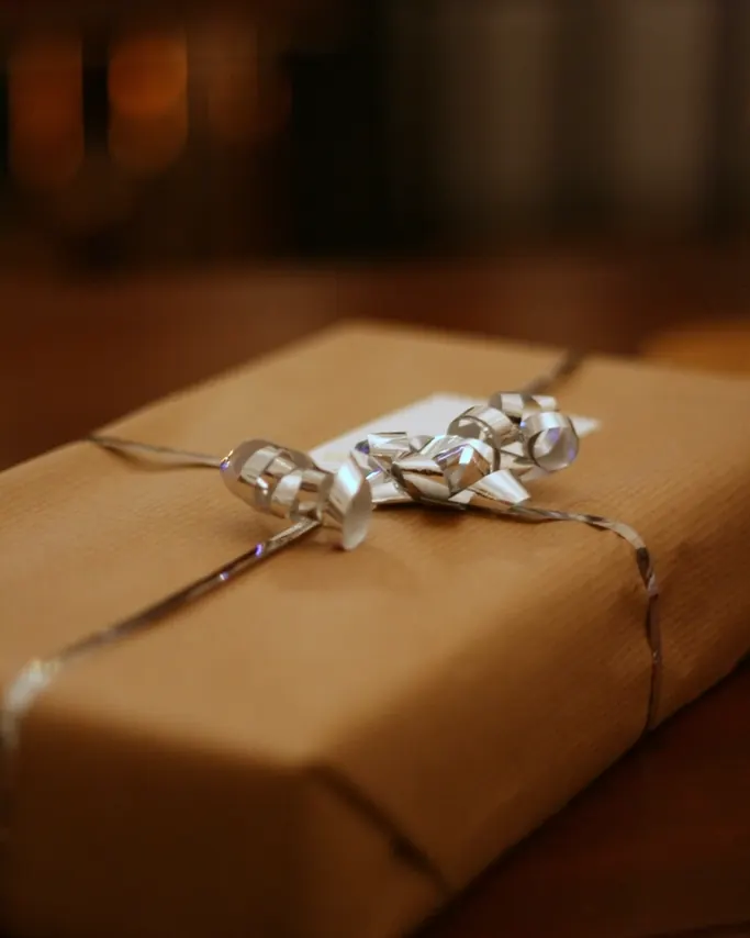A gift wrapped in plain brown kraft paper with silver ribbon on a wooden table in warm light