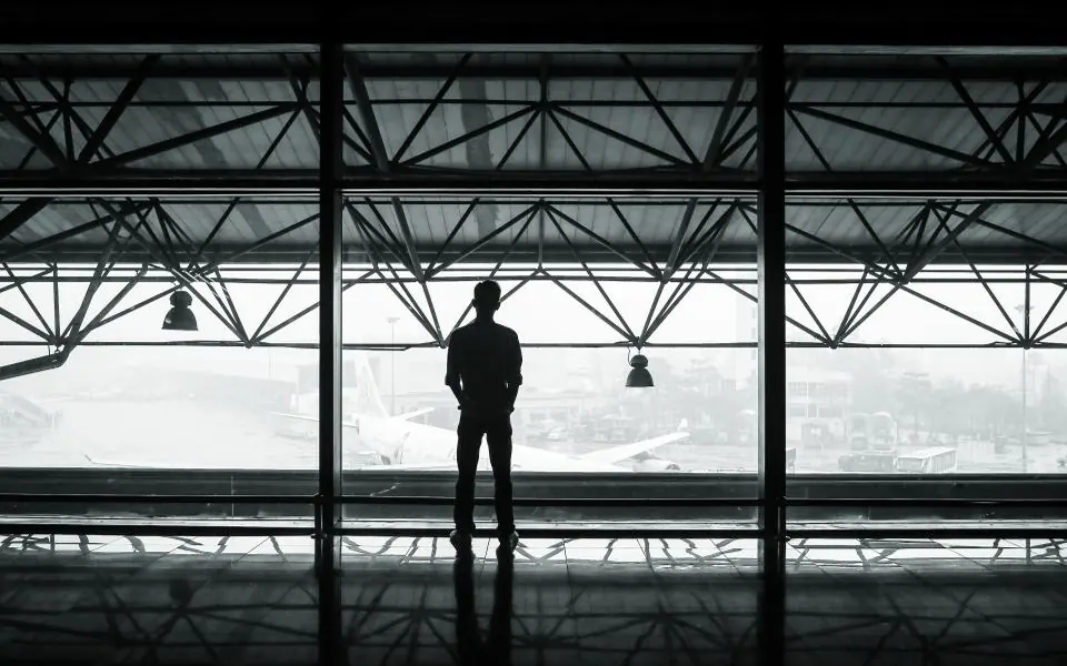 The silhouette of a man standing at a big airport window, looking out at the planes on a grey day