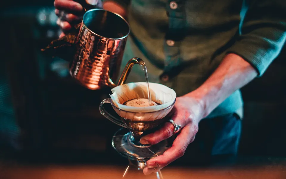 A man pouring hot water from a copper kettle into a glass pour-over coffee maker