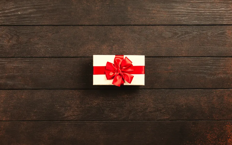 A single small white gift box tied with a red ribbon on a dark wooden table