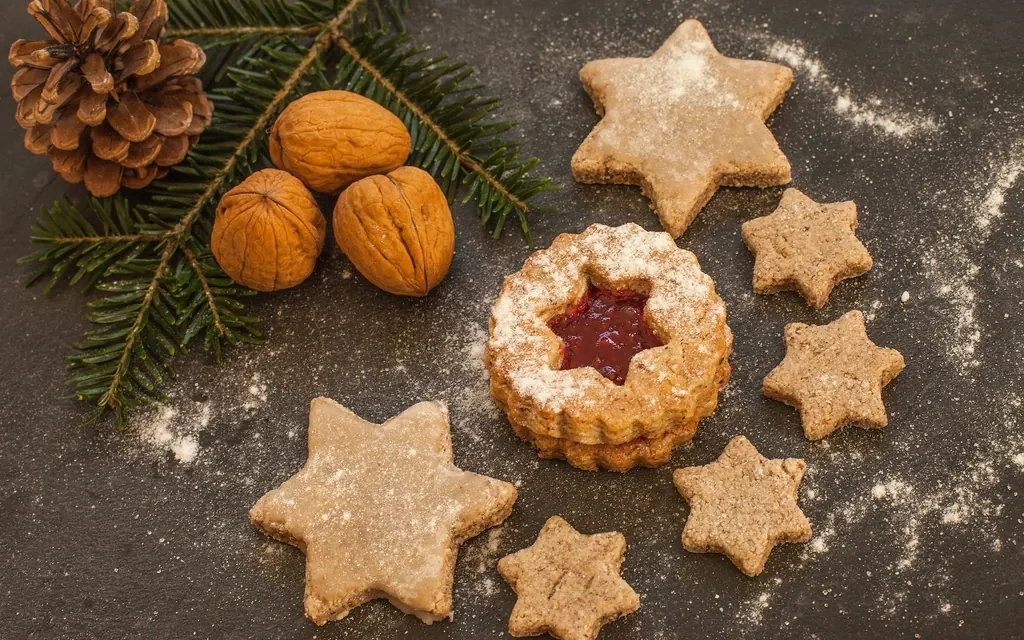 Star shaped Christmas cookies with powdered sugar next to walnuts, pine cones and fir branches on a dark table