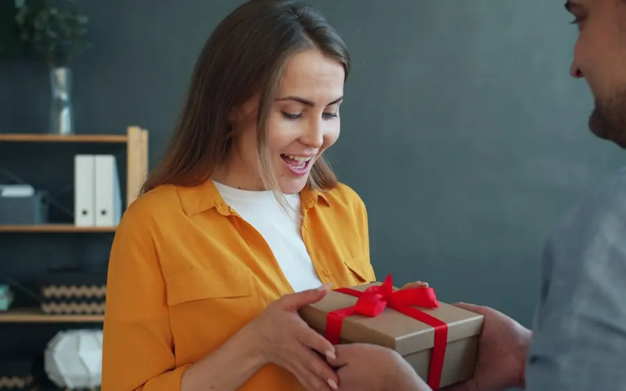 A woman smiling as her husband hands her a birthday gift
