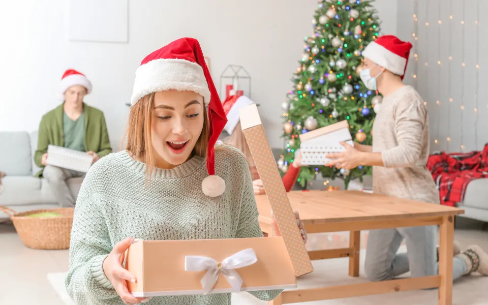 A smiling woman opening a Christmas present at home